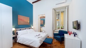 Een moderne slaapkamer met een groot bed, een blauwe fauteuil en een bureau met decoratieve spullen.