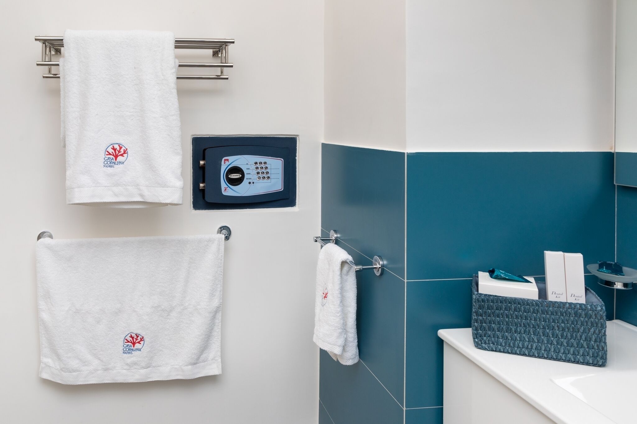 Een badkamer met twee witte handdoeken aan een metalen rek, een handdoekwarmer, en een blauwe handdoekwarmer.