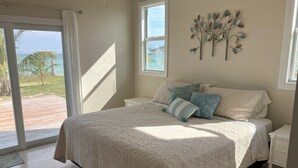 Un dormitorio con una cama grande, vista al océano a través de una puerta corrediza y un adorno de pared.