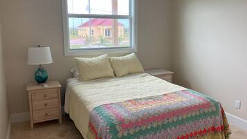 A bedroom with a bed, a nightstand, a lamp, and a window with a view of a house.
