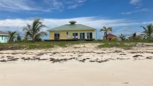 Una casa amarilla con techo verde, un porche cubierto y vista a la playa.