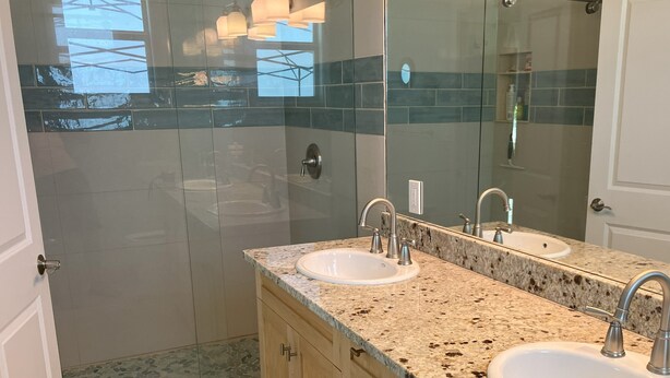 Un baño con dos lavamanos, cabina de ducha de cristal y un espejo grande.