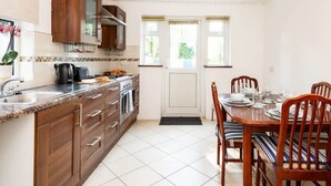A kitchen with wooden cabinets, a countertop, a stove, and a dining table with chairs. - Hanwell Private Single Room Near Station by Omega (London)