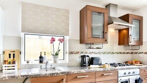 A modern kitchen with a granite countertop, wooden cabinets, a stainless steel range hood, and a window with a view of pink orchids. - Hanwell Private Single Room Near Station by Omega (London)