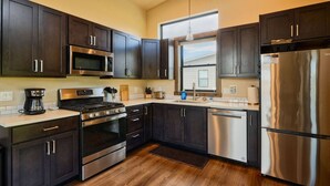 A modern kitchen with dark cabinets, stainless steel appliances, and a wooden floor.