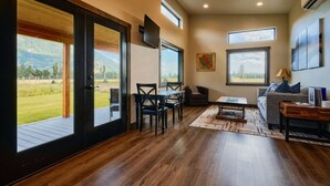 A spacious living room with a large sliding glass door leading to a deck, a cozy seating area with a sofa and chairs, and a flat-screen TV mounted on the wall.