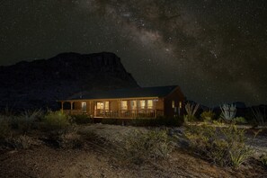 A wooden cabin with a porch, surrounded by desert vegetation, under a starry night sky. - Lodge - 3Bedrooms + 2.5 Baths in Terlingua (Terlingua)