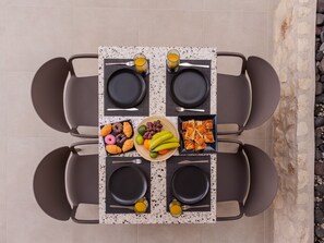 A table set for four with plates, cutlery, and a variety of food including fruits, pastries, and a glass of juice.