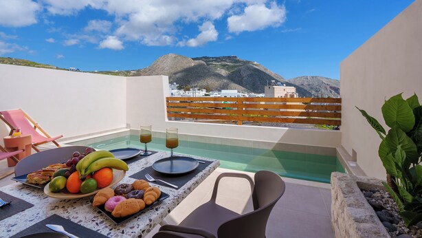 A rooftop terrace with a dining table set for breakfast, a pool, and a view of a mountain. - Sugarwhite Suites (Santorini)