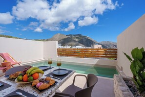 Una terraza en la azotea con mesa lista para el desayuno, piscina y vista a la montaña.