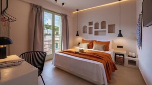 A modern bedroom with a large bed, a desk, and a chair. There is a window with curtains, a wall-mounted shelf, and a hanging light fixture. - Sugarwhite Suites (Santorini)