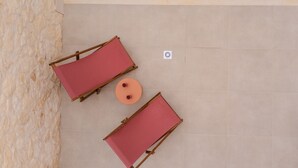 An aerial view of a pool area with two red lounge chairs and a round table. - Sugarwhite Suites (Santorini)
