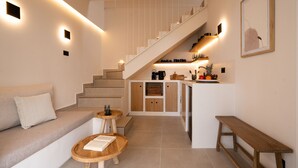 A modern living room with a staircase, a sofa, a coffee table, and a bench. - Sugarwhite Suites (Santorini)