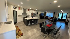 A modern kitchen with a central island, dining area with a round table and chairs, and a living room with a sofa and TV. - Gulf Breeze Retreat#Beaches#vacation rental. (Gulf Breeze)