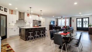 A modern kitchen with white cabinets, a central island with stools, and a dining area with a table and chairs. - Gulf Breeze Retreat#Beaches#vacation rental. (Gulf Breeze)