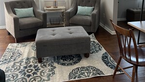 Un salon avec deux fauteuils, une table basse, une lampe et une horloge au mur.