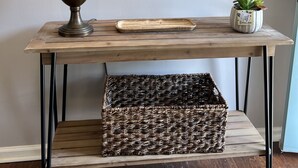 Une console en bois agrémentée d’une lampe, d’un miroir, d’un plateau, d’une plante en pot et d’un panier en osier.