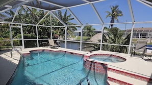 A pool with a clear blue water feature, surrounded by a covered area with chairs and a table.