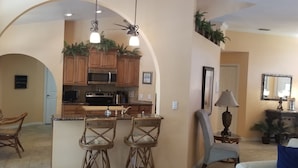A spacious kitchen with wooden cabinets, a central island with bar stools, and a ceiling fan.