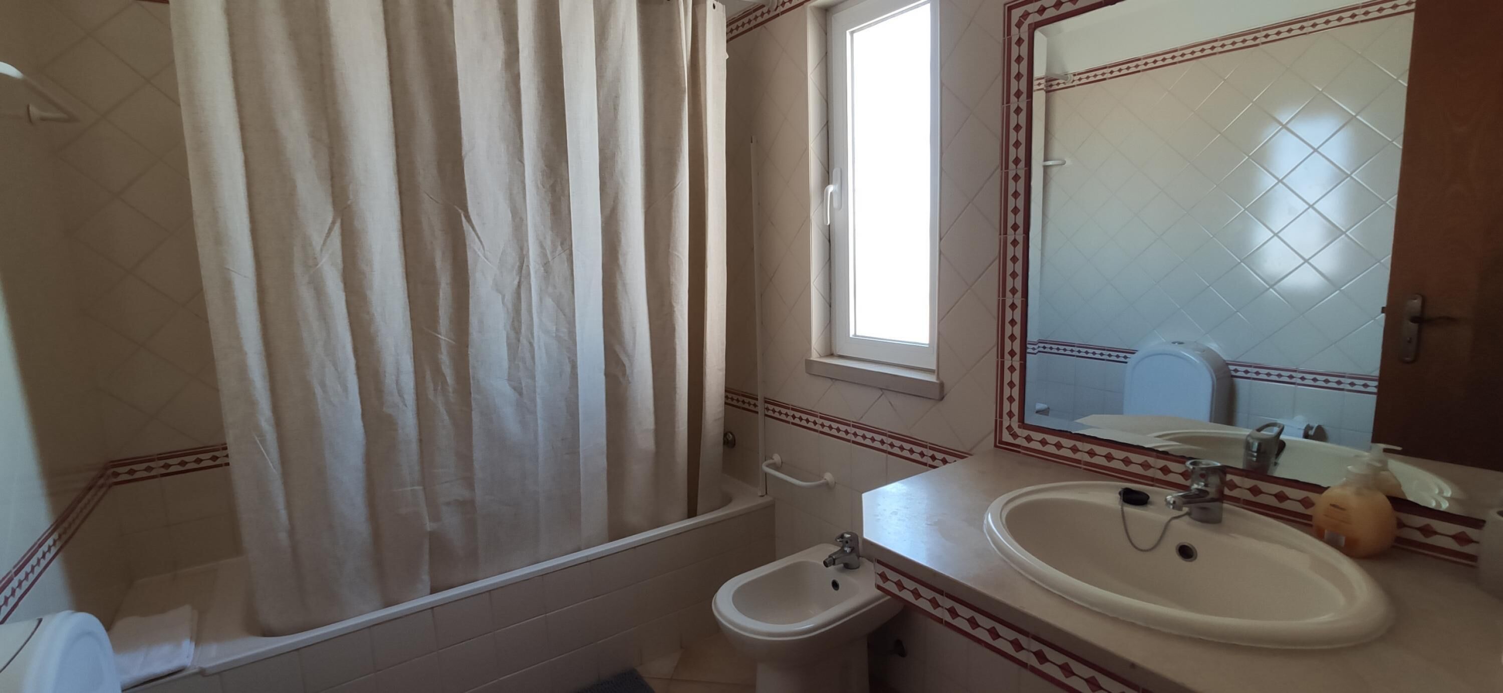 A bathroom with a bathtub, a sink, a mirror, and a window.