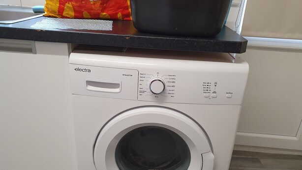 Una lavadora de carga frontal con un panel de control, una olla negra encima y una bolsa de detergente.