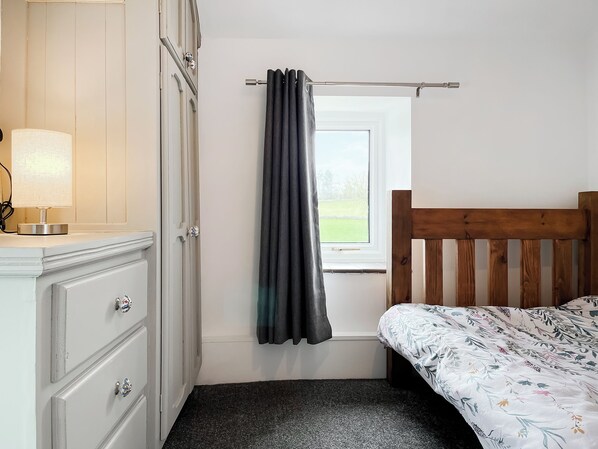 Une chambre à coucher avec une tête de lit en bois, une fenêtre avec des rideaux, une table de chevet avec une lampe et une commode avec des tiroirs.