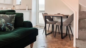 Ein gemütlicher Wohnbereich mit einem grünen Sofa, einem Holzesstisch mit zwei Stühlen und einer Küche im Hintergrund.