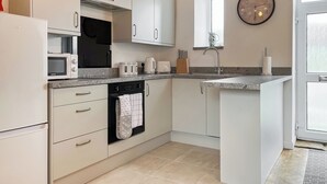 Eine moderne Küche mit weißen Schränken, einem Einbauofen, einer Mikrowelle, einer Kaffeemaschine und einem Spülbecken.