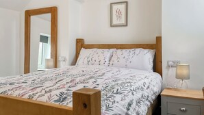 Ein Schlafzimmer mit einem Bettgestell aus Holz, blumigem Bettzeug, einem Nachttisch mit Lampe und einem gerahmten Bild an der Wand.