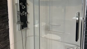 En dusch med glasväggar, utrustad med ett duschhuvud som kan hållas i handen, ett löstagbart duschmunstycke och en handhållen massageapparat.