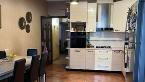 A modern kitchen with white cabinets, a gas stove, and a refrigerator. There is a dining area with a table and chairs. - Deluxe seaside Batumi  (Batumi)