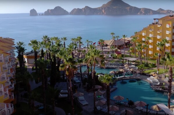 A resort with a pool, palm trees, and a view of the ocean.