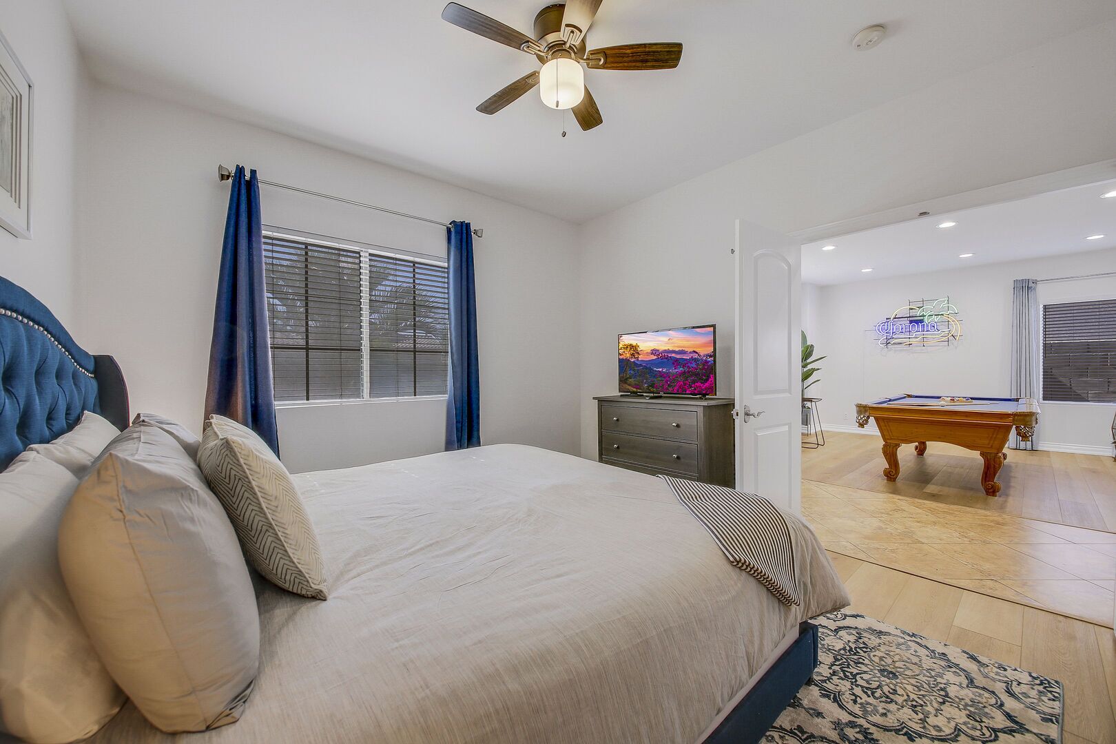 A bedroom with a bed, a television, a ceiling fan, and a pool table in the adjacent room.