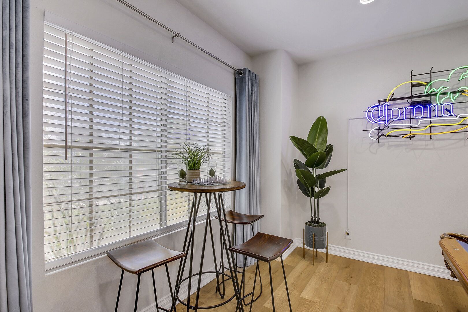 Een moderne kamer met een groot raam, een neonbord, een ronde tafel met stoelen en een potplant.