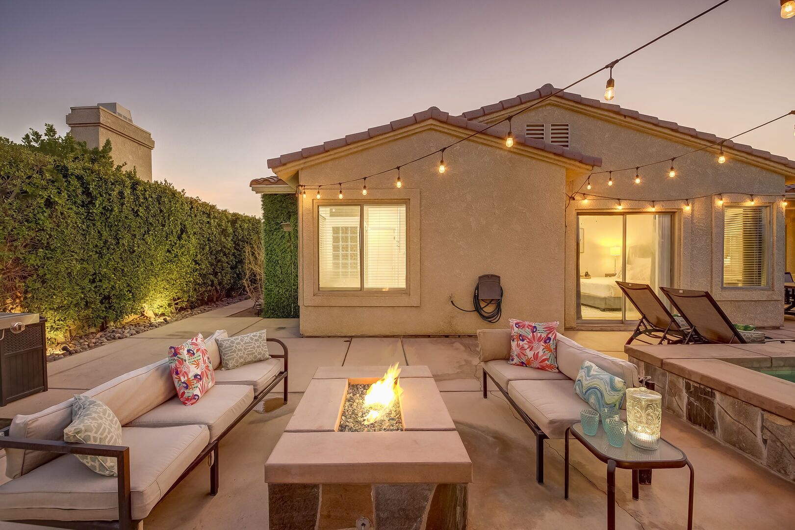 A patio area with a fire pit, outdoor seating, and string lights.