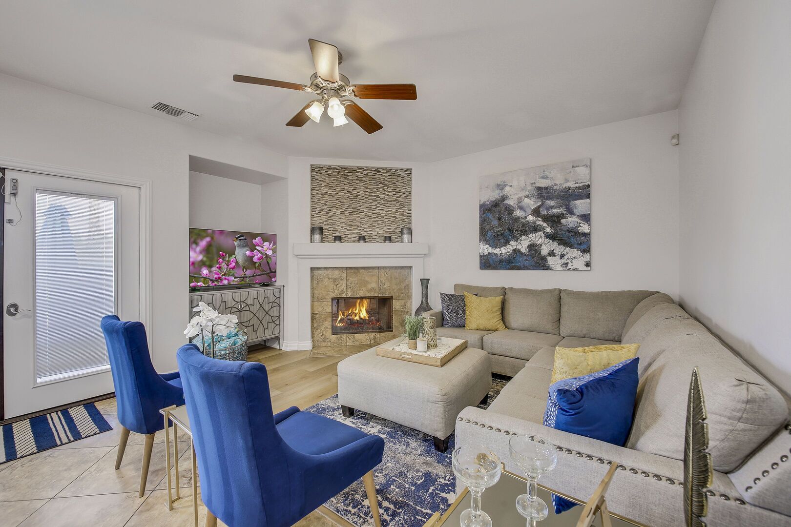 A modern living room with a fireplace, a ceiling fan, and a large window.