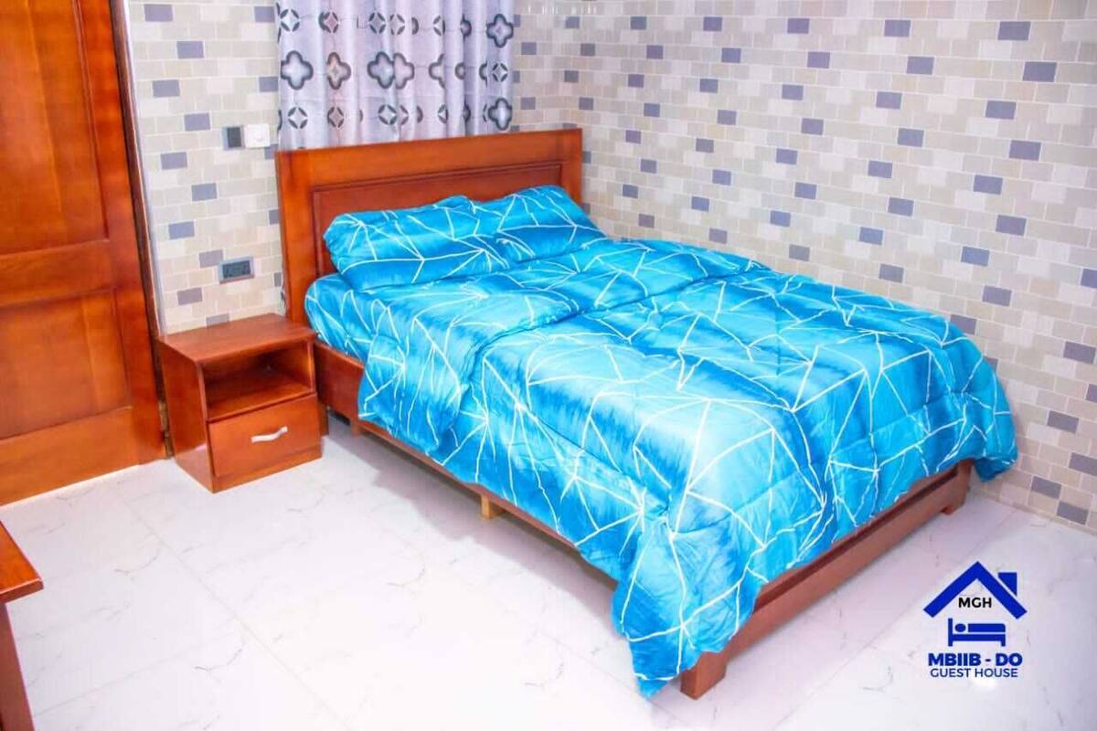 Quarto com cama de madeira, mesa de cabeceira e uma gaveta pequena.