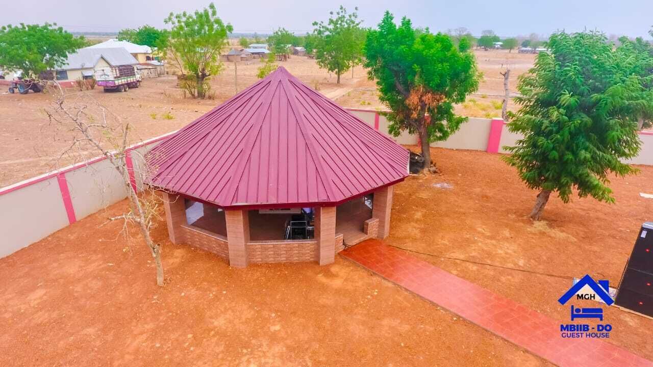 Ein kleines Gästehaus mit rotem Dach, umgeben von einer unbefestigten Fläche und spärlicher Vegetation.