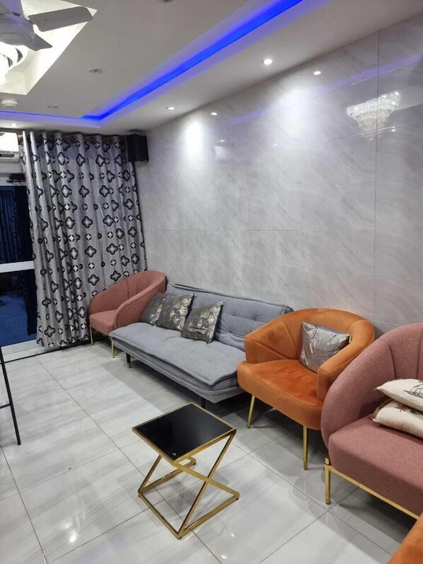 A modern living room with a grey sofa, orange armchairs, and a black coffee table with gold legs.