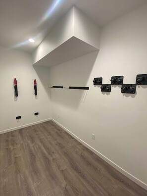 Una habitación con techo inclinado, piso de madera y una repisa de pared con objetos negros.