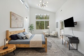A modern bedroom with a wooden bed, a desk, a TV, and large windows.