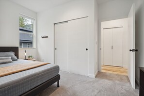 A bedroom with a bed, a bedside table, a lamp, a window, and a door. - Sandy River Group Getaway 2 (Mount Hood Village)