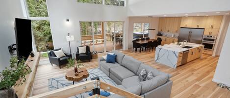 Amplia sala de estar con un sofá gris, piso de madera y una zona de comedor con mesa y sillas.