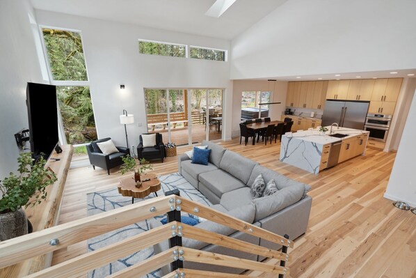 A spacious living area with a grey sofa, wooden flooring, and a kitchen with modern appliances.