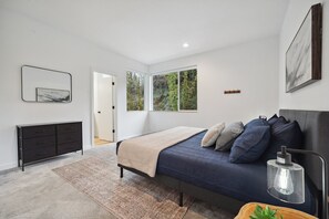 Un dormitorio moderno con cama, mesita de noche y vistas al verdor a través de amplios ventanales.