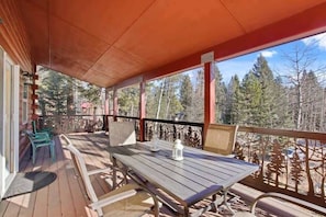A covered outdoor area with a wooden table and chairs, a railing, and a view of trees. - Mountain Getaway, Pet friendly (McCall)