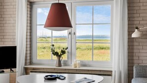 Ein Zimmer mit einem großen Fenster, einer roten Pendelleuchte, einem kleinen Tisch mit Blumenvase und einem Sessel.