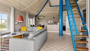 Ein zeitgemäßer Wohnbereich mit grauem Sofa, einem farbenfrohen Streifen Teppich, einer Holztreppe und einem Küchenbereich.