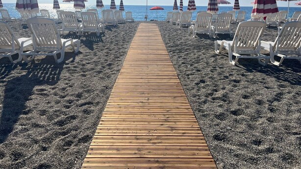 Een strand met een houten looppad dat leidt naar rijen witte ligbedden en gestreepte strandparasols.