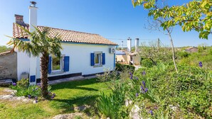 Un bâtiment blanc avec un toit recouvert de tuiles, un palmier et des fleurs violettes au premier plan.